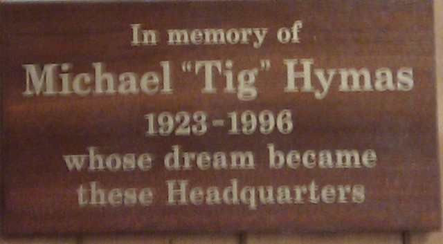 Wooden memorial plaque stating: In memory of Michael 'Tig' Hymas 1923-1996 whose dream became these Headquarters.